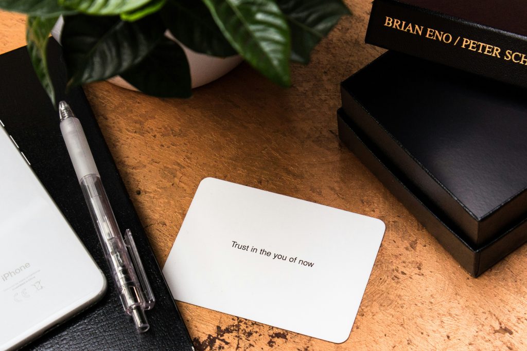 A card on a table says "trust in the you of now"